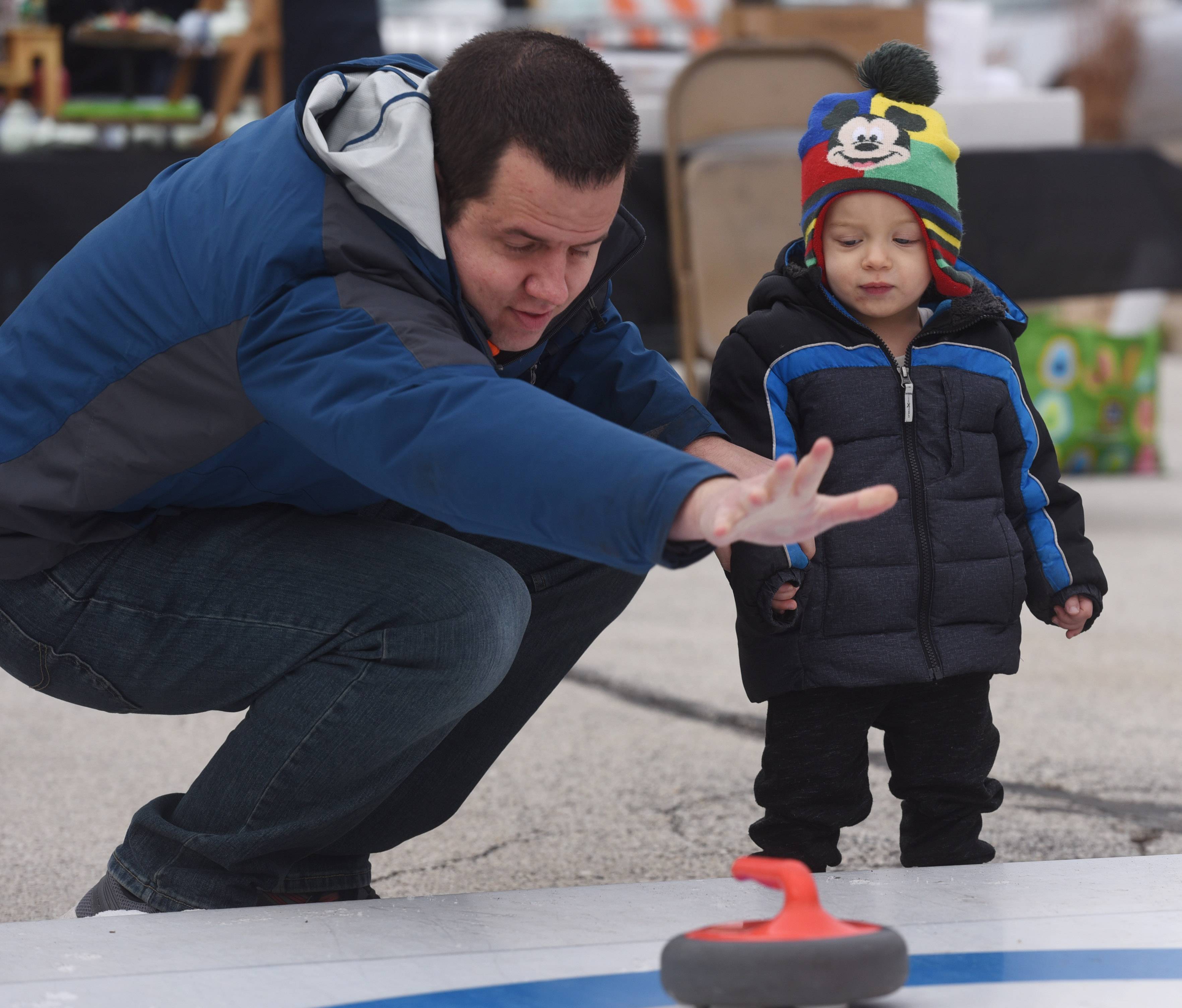 Chris Lalla of Oak Brook demonstrates curling for his son, Mason, 1, during Frozen Fest Saturday in Glen Ellyn.